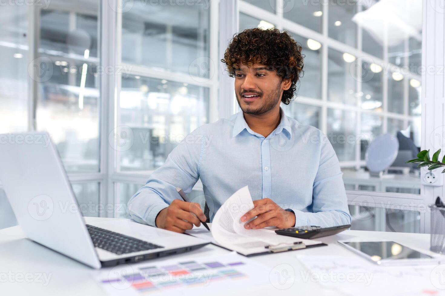 alegre y exitoso Hispano empresario en papel trabajar, hombre firma facturas y contratos, joven jefe gerente a lugar de trabajo con informes. foto