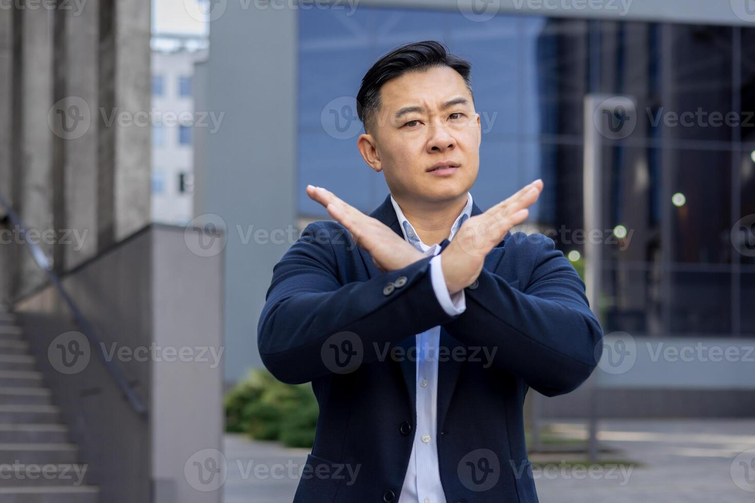 Determined male executive in smart attire gesturing prohibition with crossed arms in front of a modern building. photo