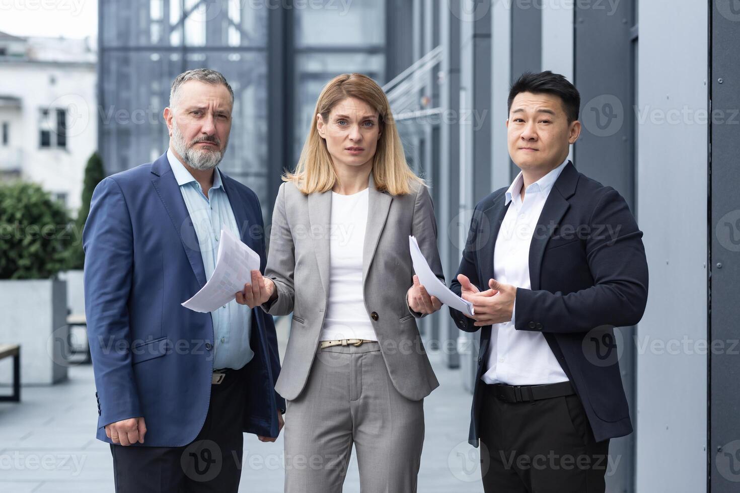 Frustrated female business boss with documents looking at camera, team of diverse colleagues outside office building upset with result of work report photo