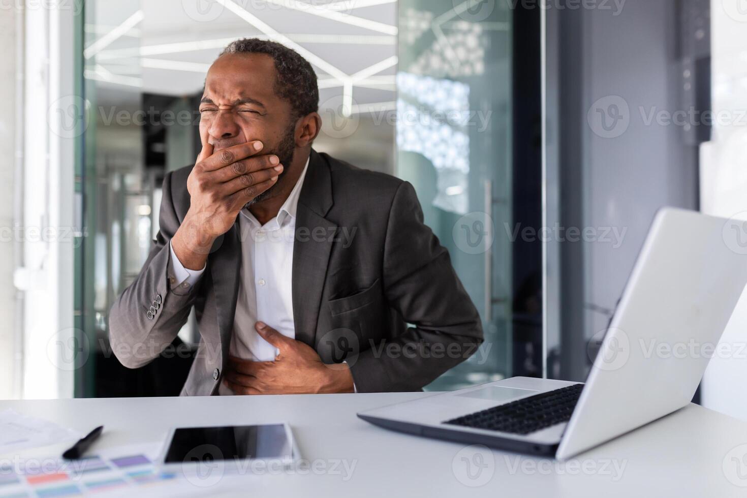 Sick man at workplace inside office, african american man got food poisoning on lunch break, businessman has nausea and burps while sitting at desk. photo