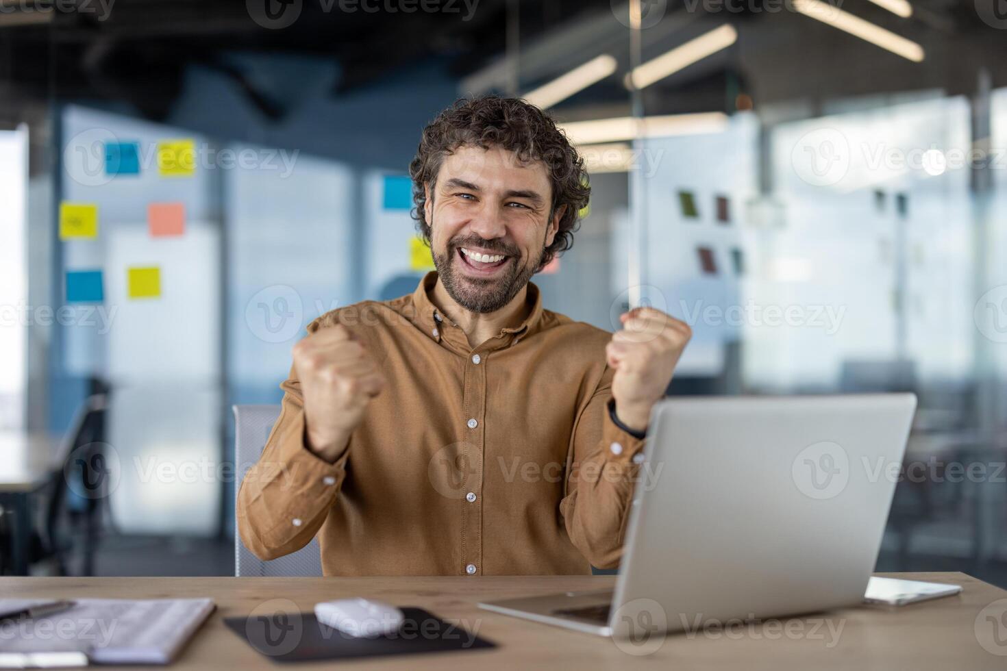 alegre masculino profesional exultante triunfo con ordenador portátil en un moderno oficina configuración, demostración positivo emociones y éxito. foto