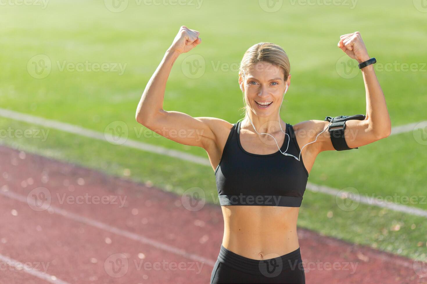 energético mujer corredor demostración fuerza y éxito con un confidente brazo aumento en un soleado atlético pista. foto