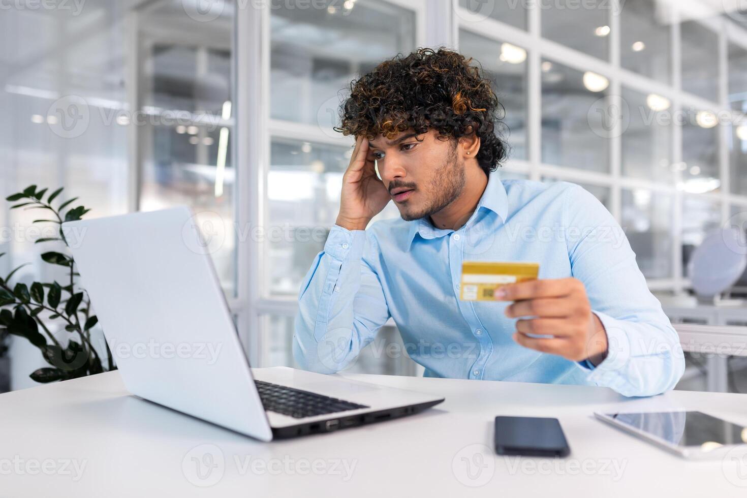 Upset and deceived businessman inside office trying to transfer money online, nervous man holding bank credit card, got rejected and error of funds on account negative balance. photo