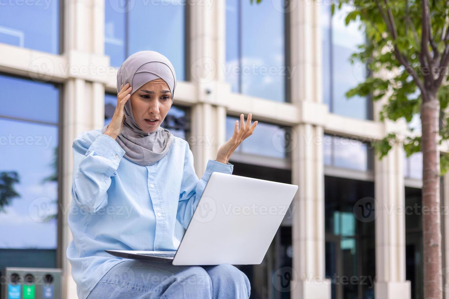 Young Muslim woman in a hijab looking confused while using a laptop on a university campus, showing frustration and technology challenges. photo