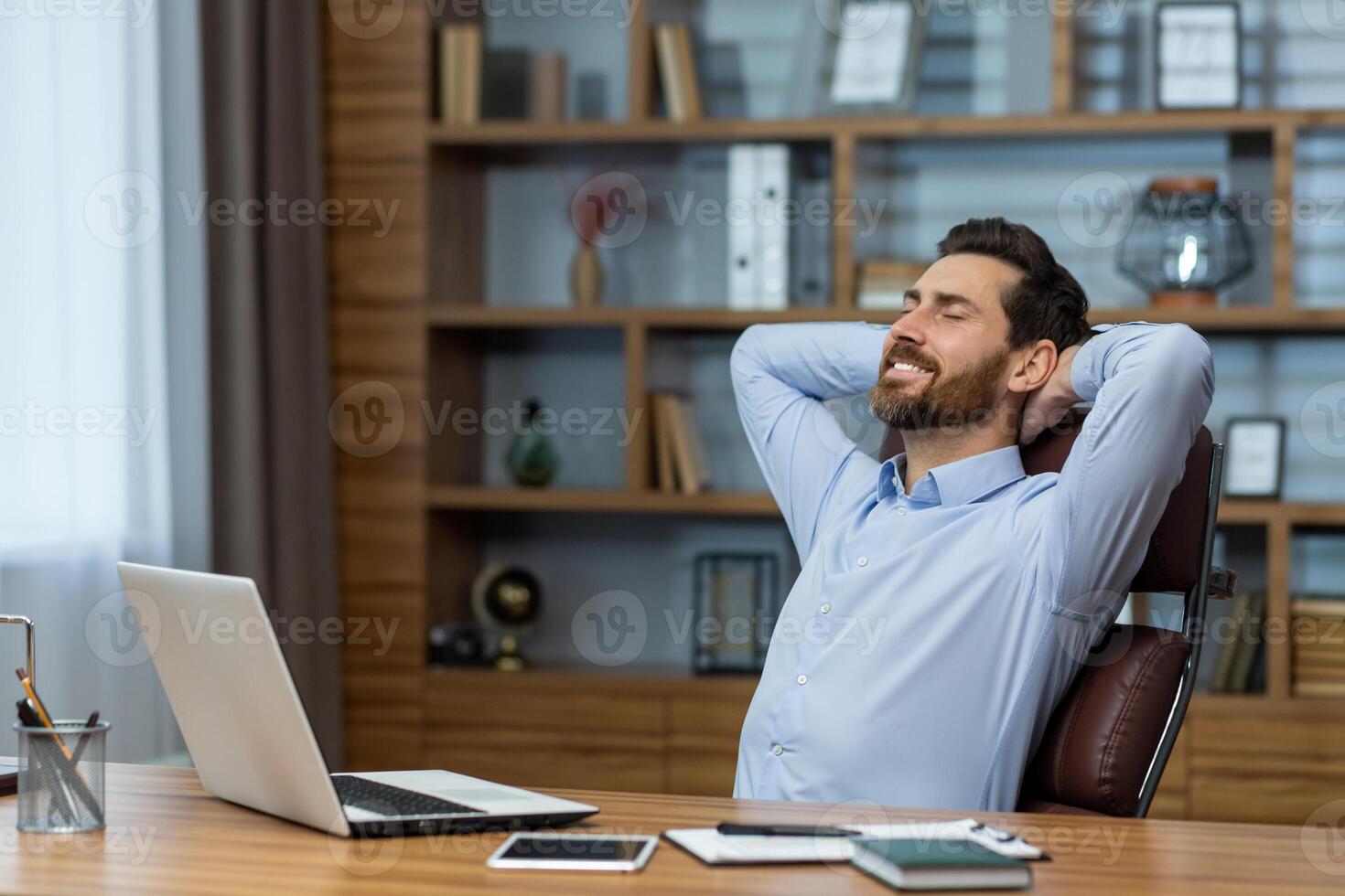 Content mature businessman taking a break, relaxing with hands behind his head in a well-organized home office setting. photo