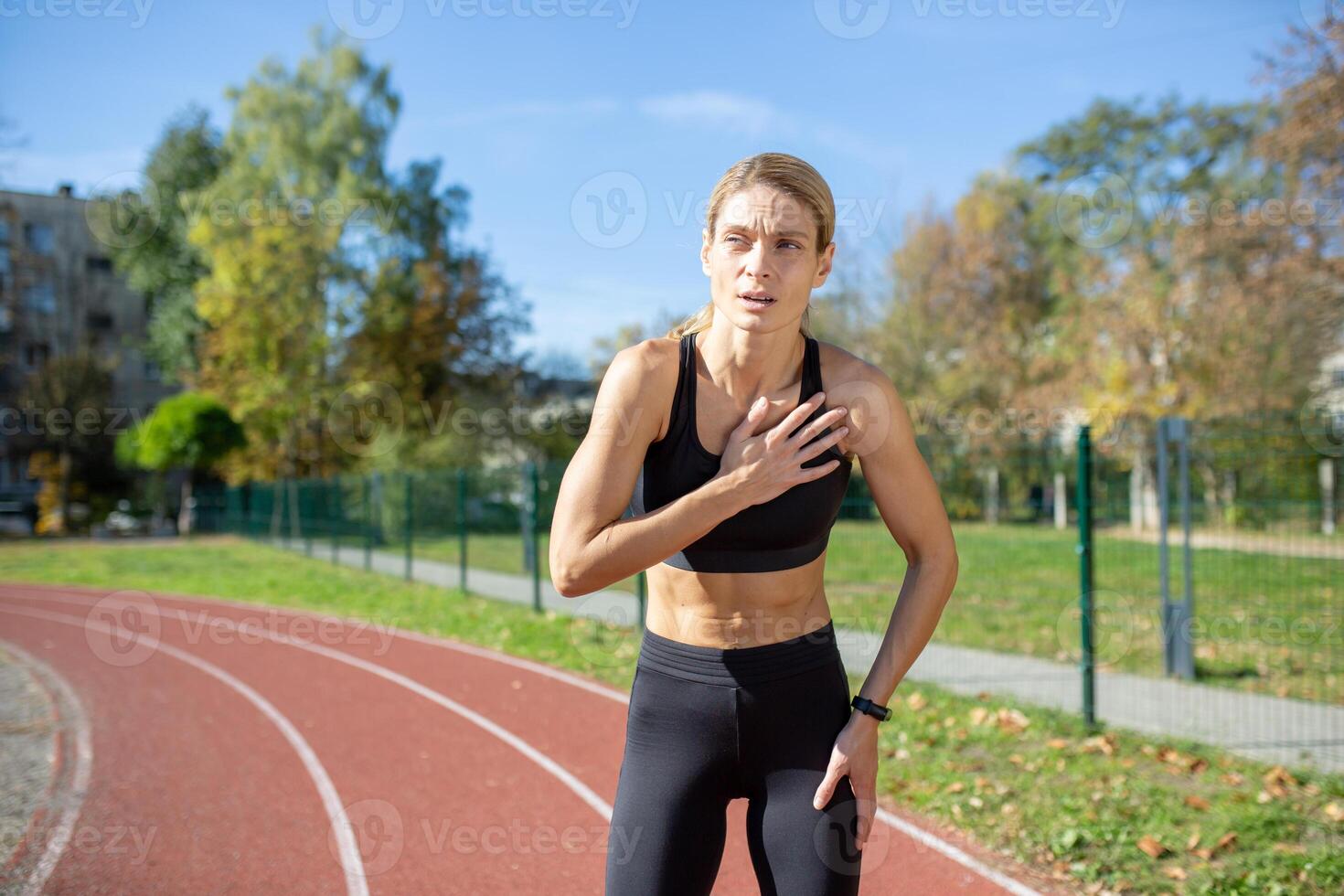 Focused sportswoman taking a break on running track, hands on knees, feeling exhaustion after sprint. Concept of determination and fitness training. photo