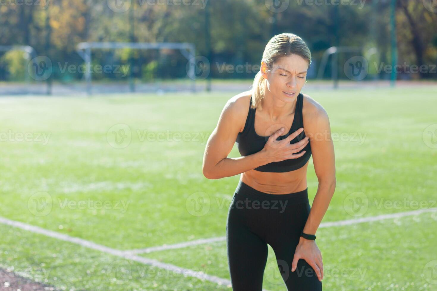 Determined woman in sportswear taking a break, catching her breath post-workout on a sunny sports field. photo