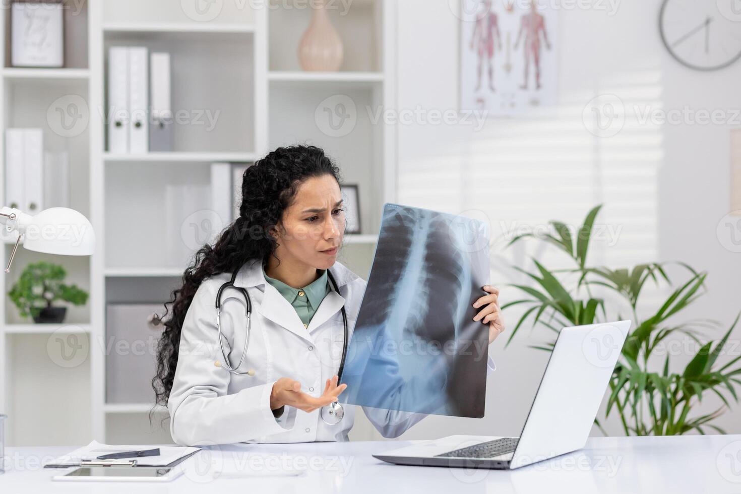 A professional female doctor examines an X-ray film, focusing intently in her modern office filled with medical charts and plants. photo