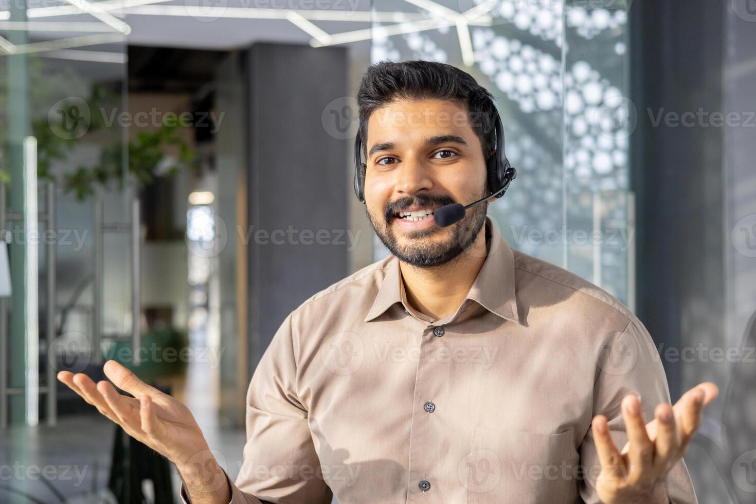 Cheerful Indian businessman wearing a headset communicating in a modern office setting. Engaged and professional, he looks directly at the camera. photo