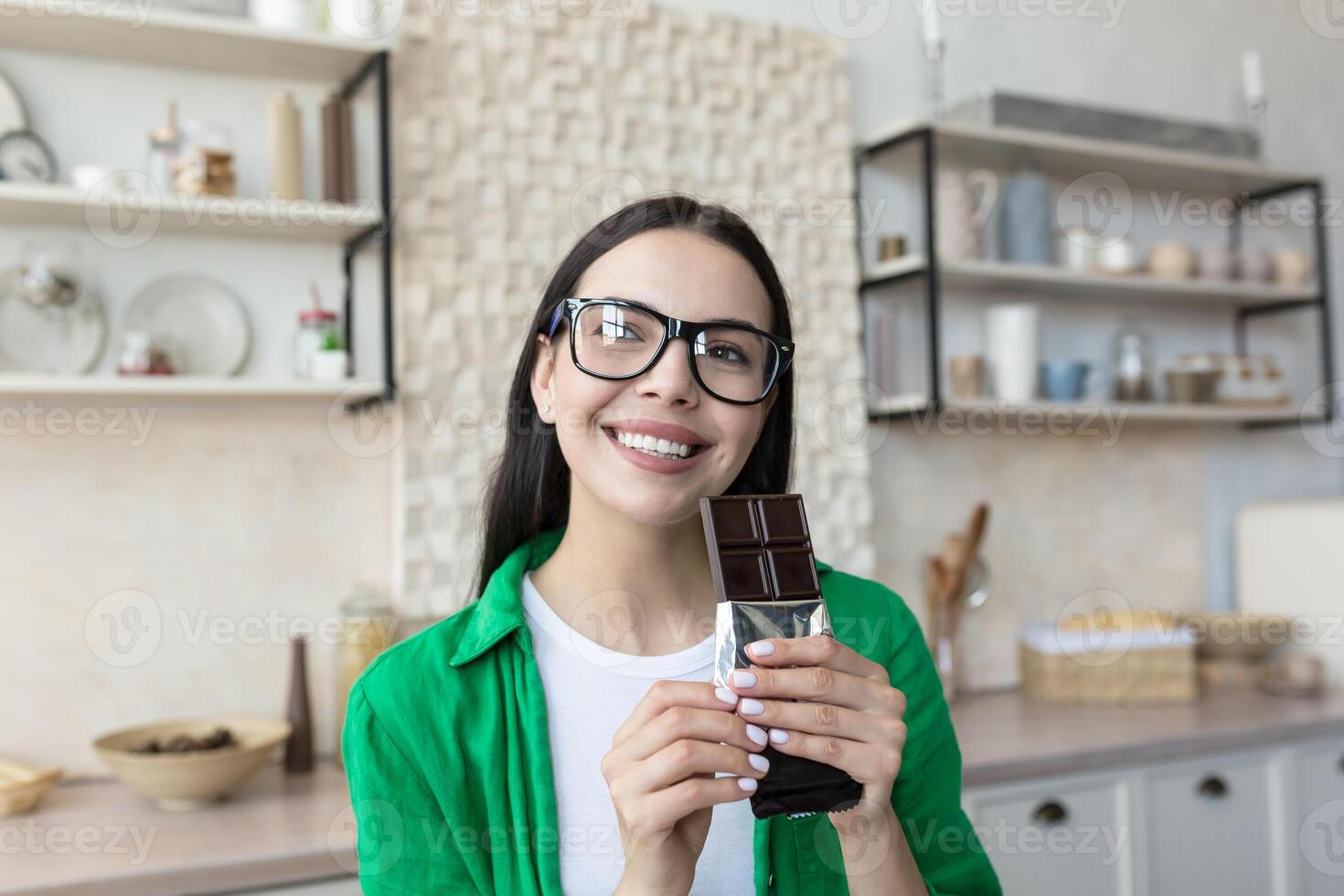 Portrait of a woman holding a bar of black chocolate in her hands. Standing at home in the kitchen photo