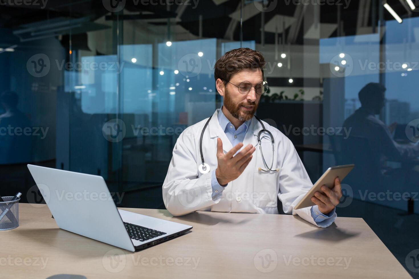 call online consultation of a doctor, an experienced doctor works inside the office of a modern clinic, gives a consultation remotely, uses a tablet to communicate photo