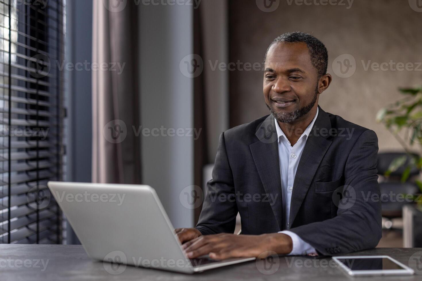 Grown up stylish man using portable gadgets for work in spacious apartment with window and plants. Progressive manager setting workspace at home and getting along with modern technology. photo