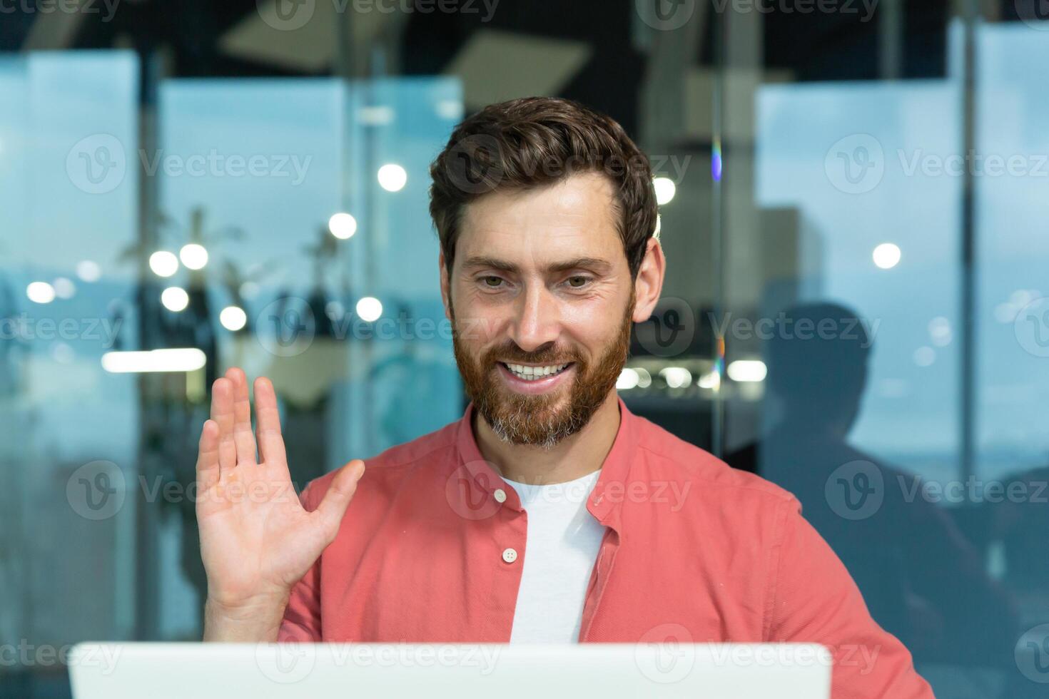 call of successful and cheerful smiling businessman, man talking remotely using laptop while sitting inside office, online meeting with colleagues and helping customers. photo