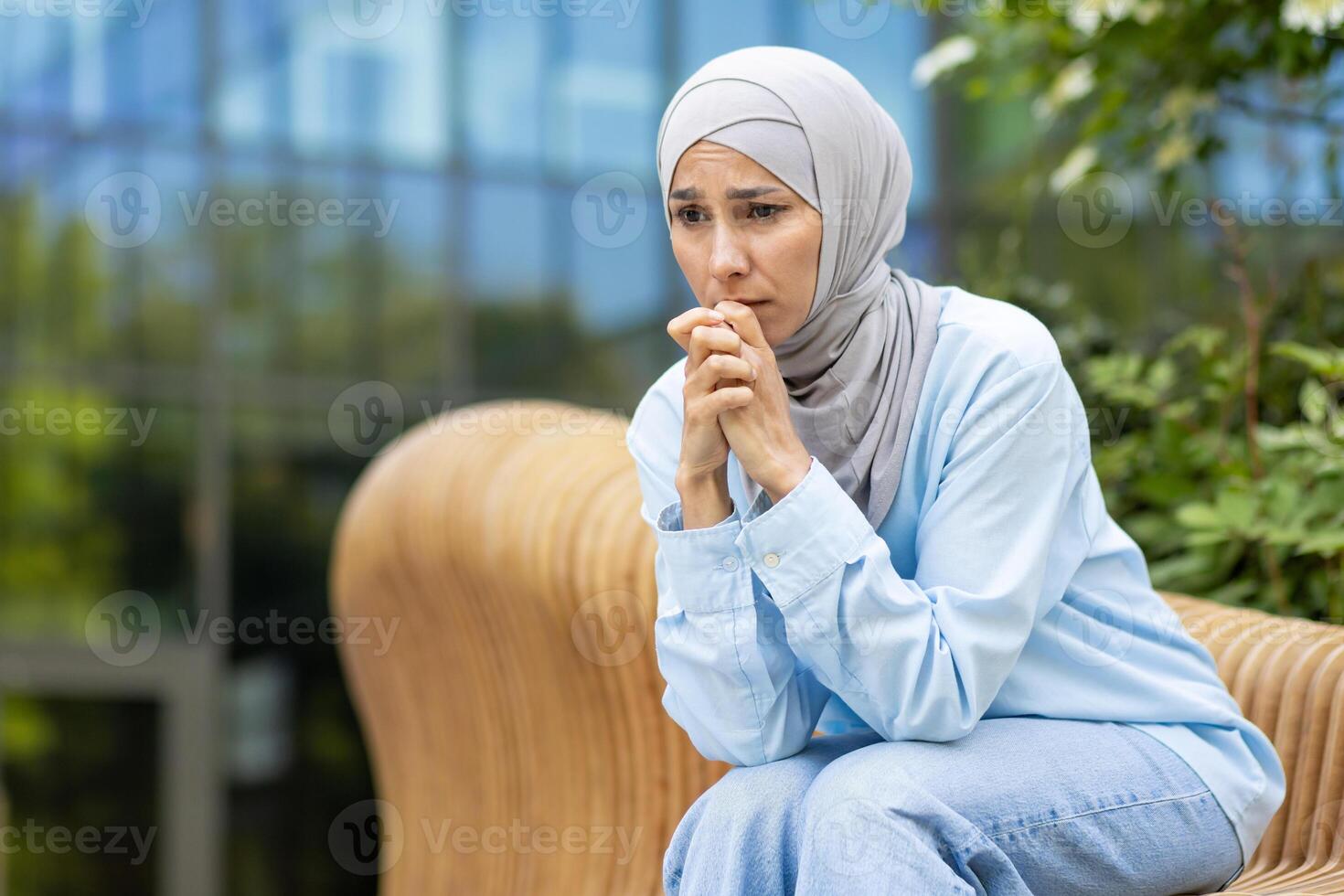 Depressed female in headscarf leaning on laps with elbows while sitting deep in thoughts with worried face. Sad lady feeling lonely and unhappy while waiting for appointment with psychotherapist. photo
