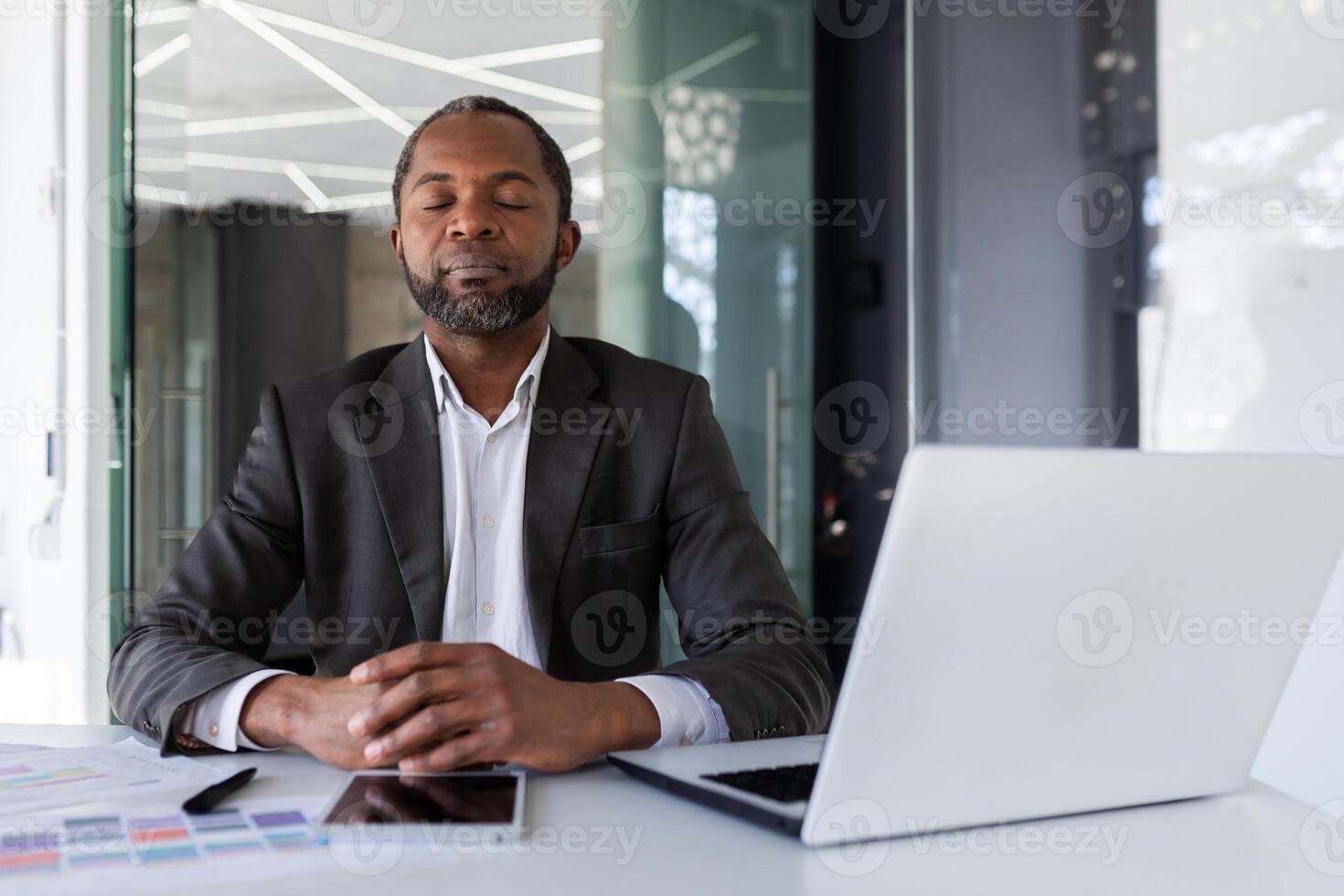 equilibrado y calma hombre a lugar de trabajo dentro oficina, empresario meditando con cerrado ojos pensando y visualizante futuro proyectos y planes financiero estrategias, jefe dentro oficina con ordenador portátil. foto