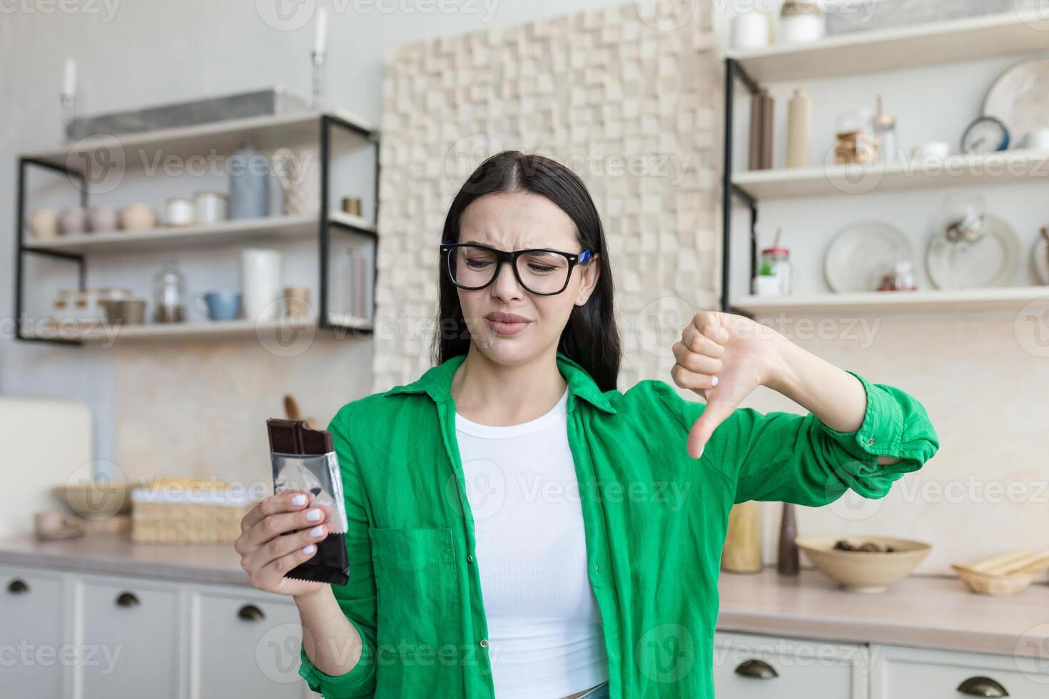 Dissatisfied woman holding a bar of chocolate in her hand and points a finger of dislike photo