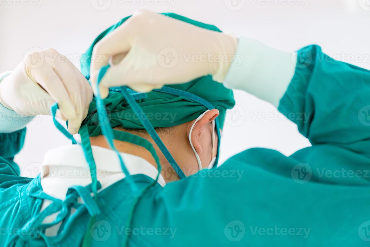Back view of surgeon tying surgical cap in preparation, Medical team performing surgical operation in operating room, Team surgeon at work in operating room photo