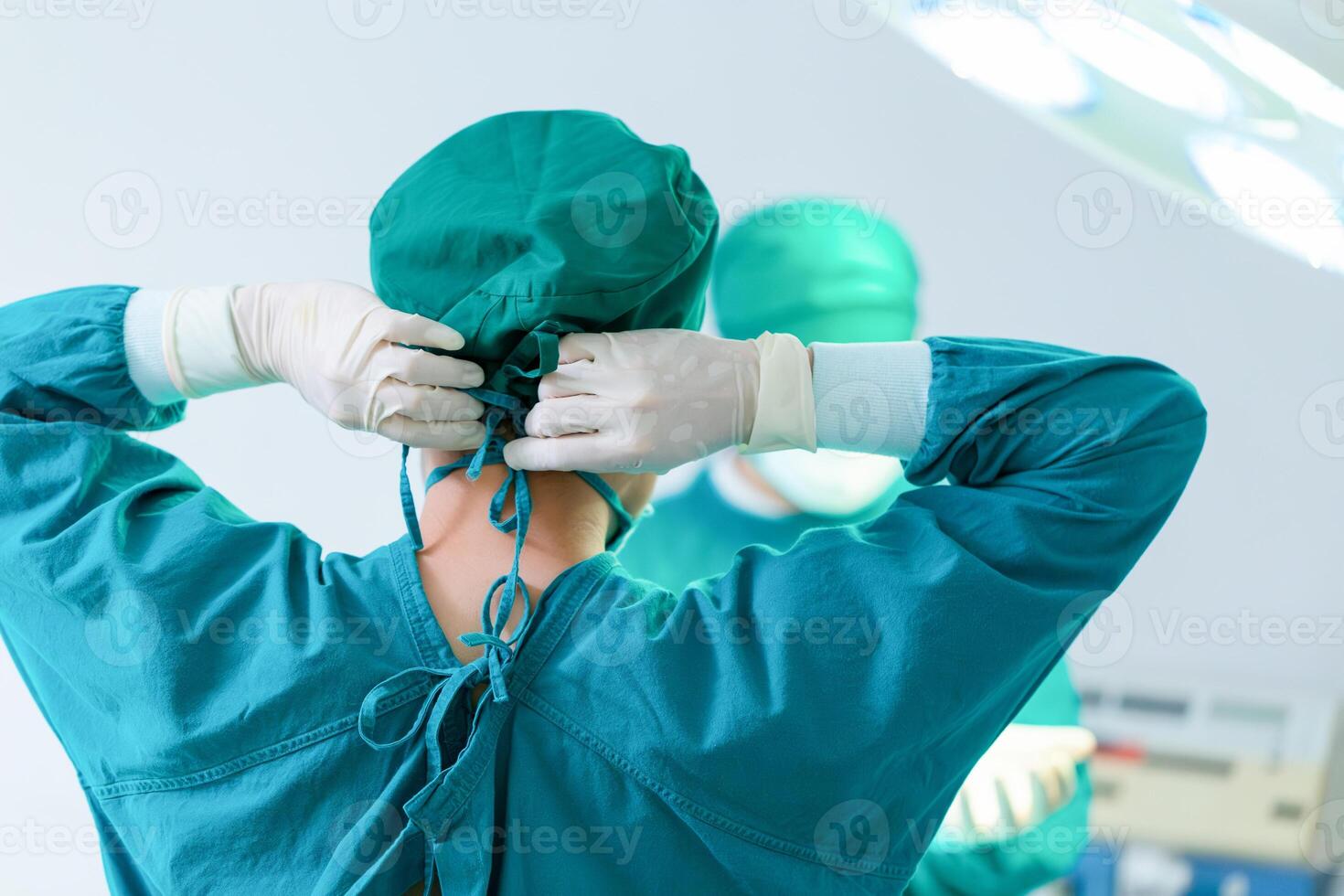 Back view of surgeon tying surgical cap in preparation, Medical team performing surgical operation in operating room, Team surgeon at work in operating room photo