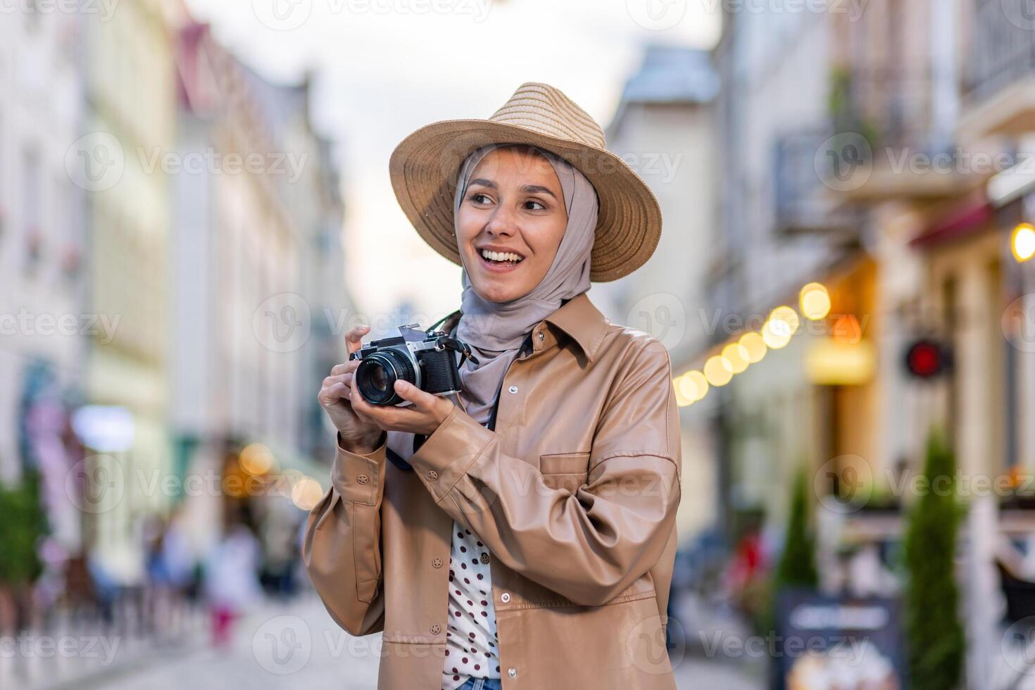 Young beautiful woman walking in the evening city in hijab, tourist with camera and wearing a hat inspects the historical city smiling with satisfaction, Muslim woman on a trip. photo
