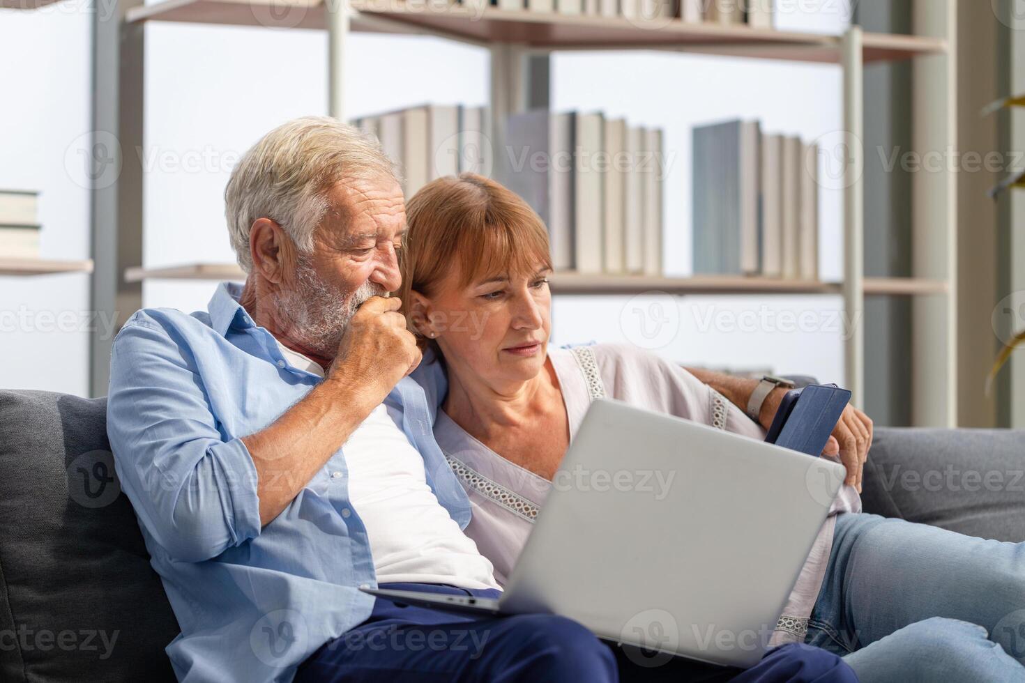 Senior couple spending time together in the living room, woman and man using laptop and digital tablet on the cozy sofa at home photo