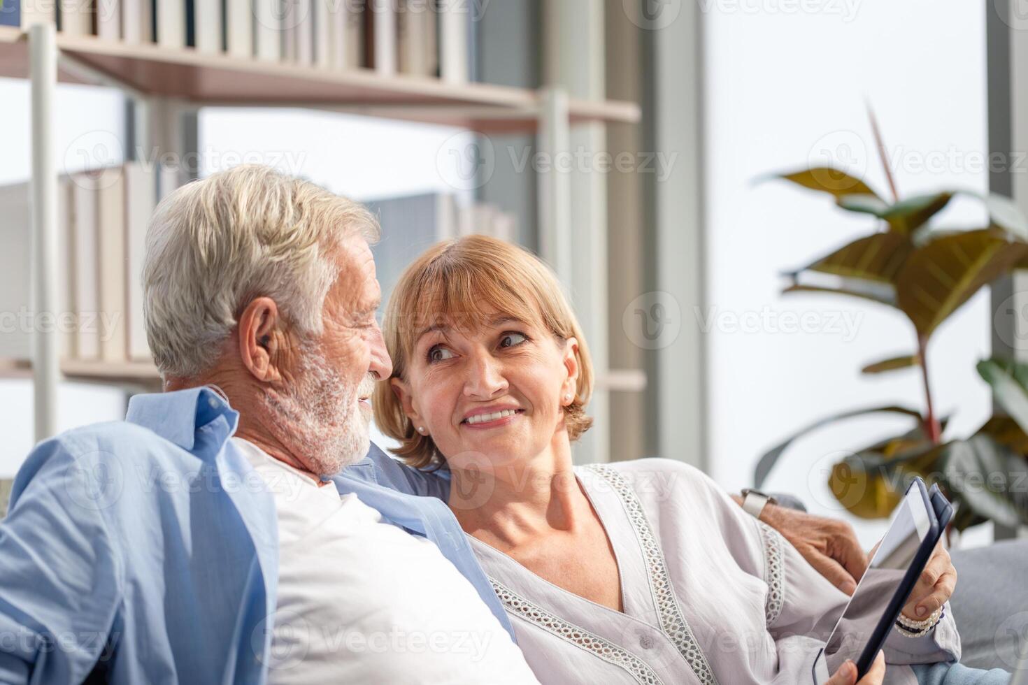 Senior couple spending time together in the living room, woman and man using digital tablet on the cozy sofa at home photo