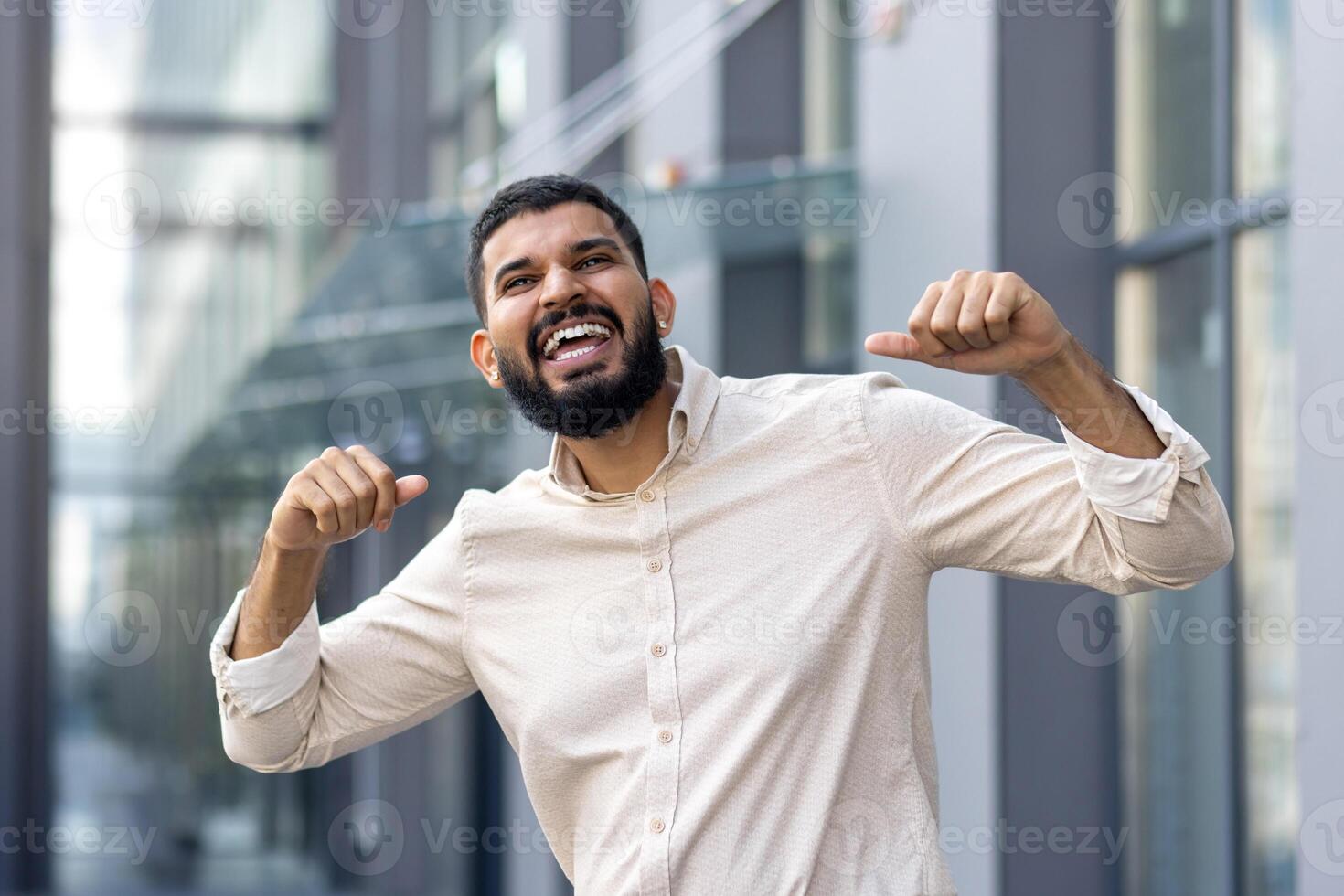 Close-up portrait of a young happy Muslim man standing outside on the street and rejoicing in good news and success, celebrating with joy and raising his hands up photo