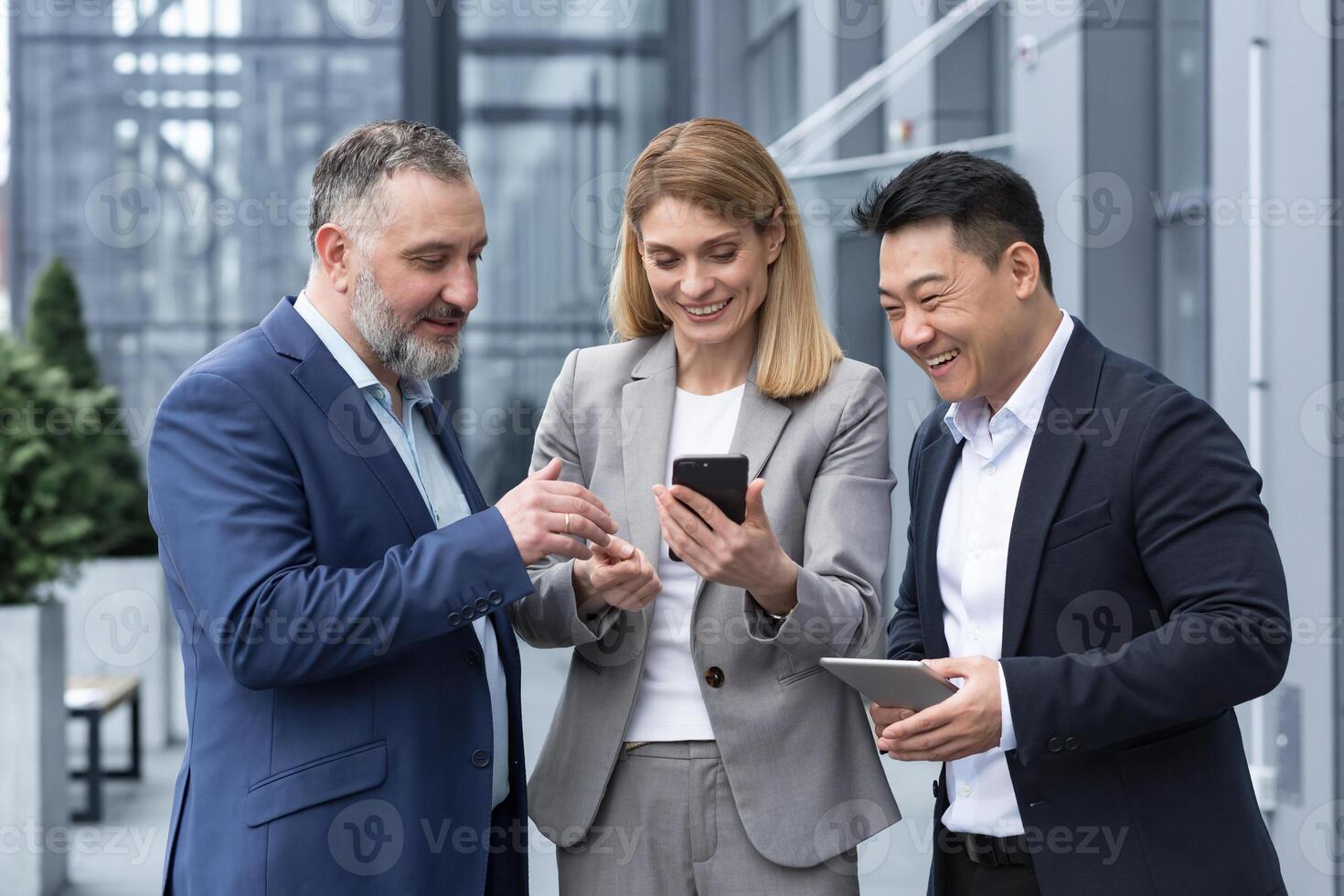 Three colleagues employees watch funny s or look at photos, pictures memories looking at smartphone screen using mobile phone. group of business people office workers having fun on breaks photo