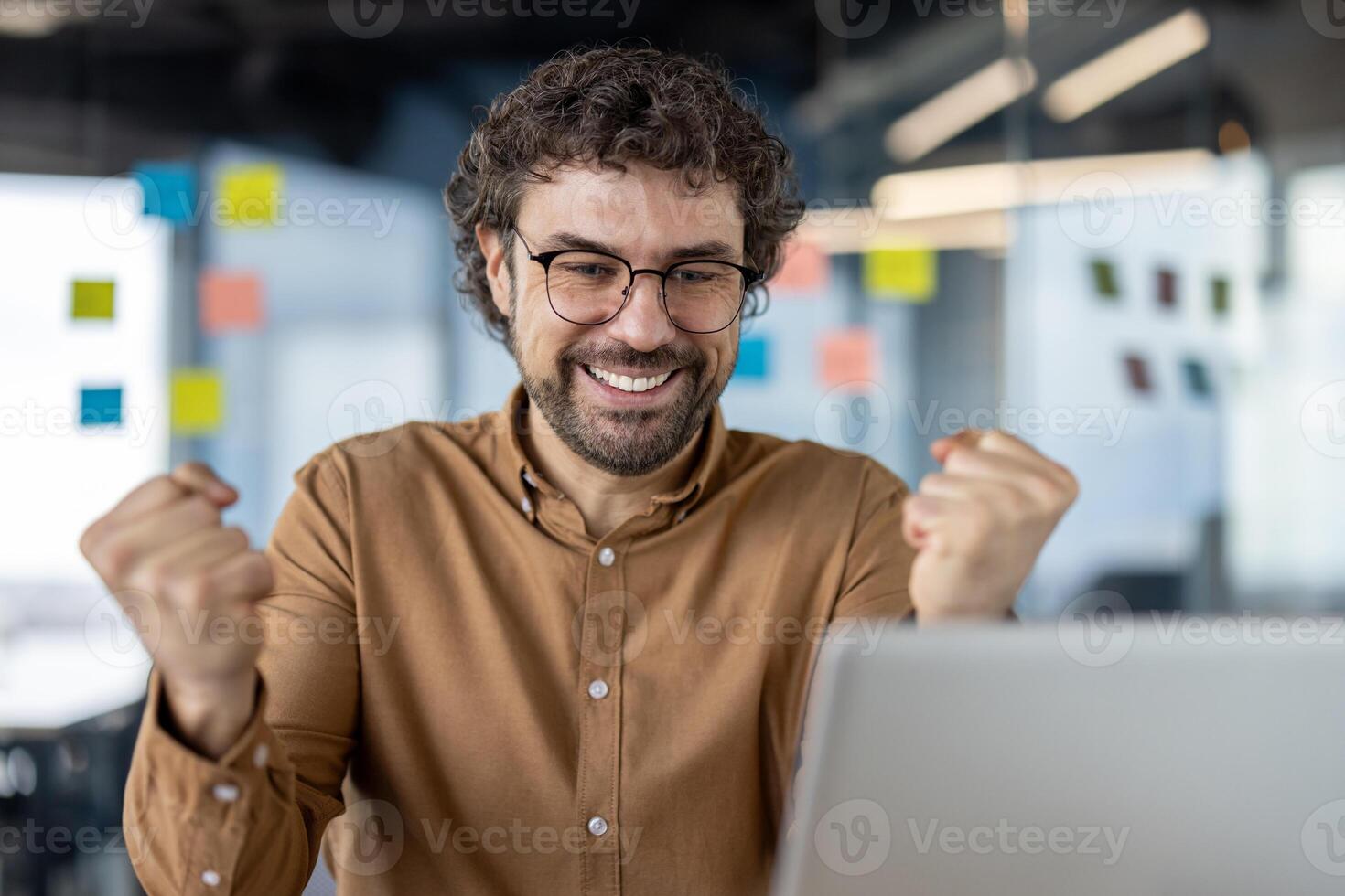 Euphoric business professional triumphantly raising fists in a jubilant gesture of success and achievement at the workplace. photo