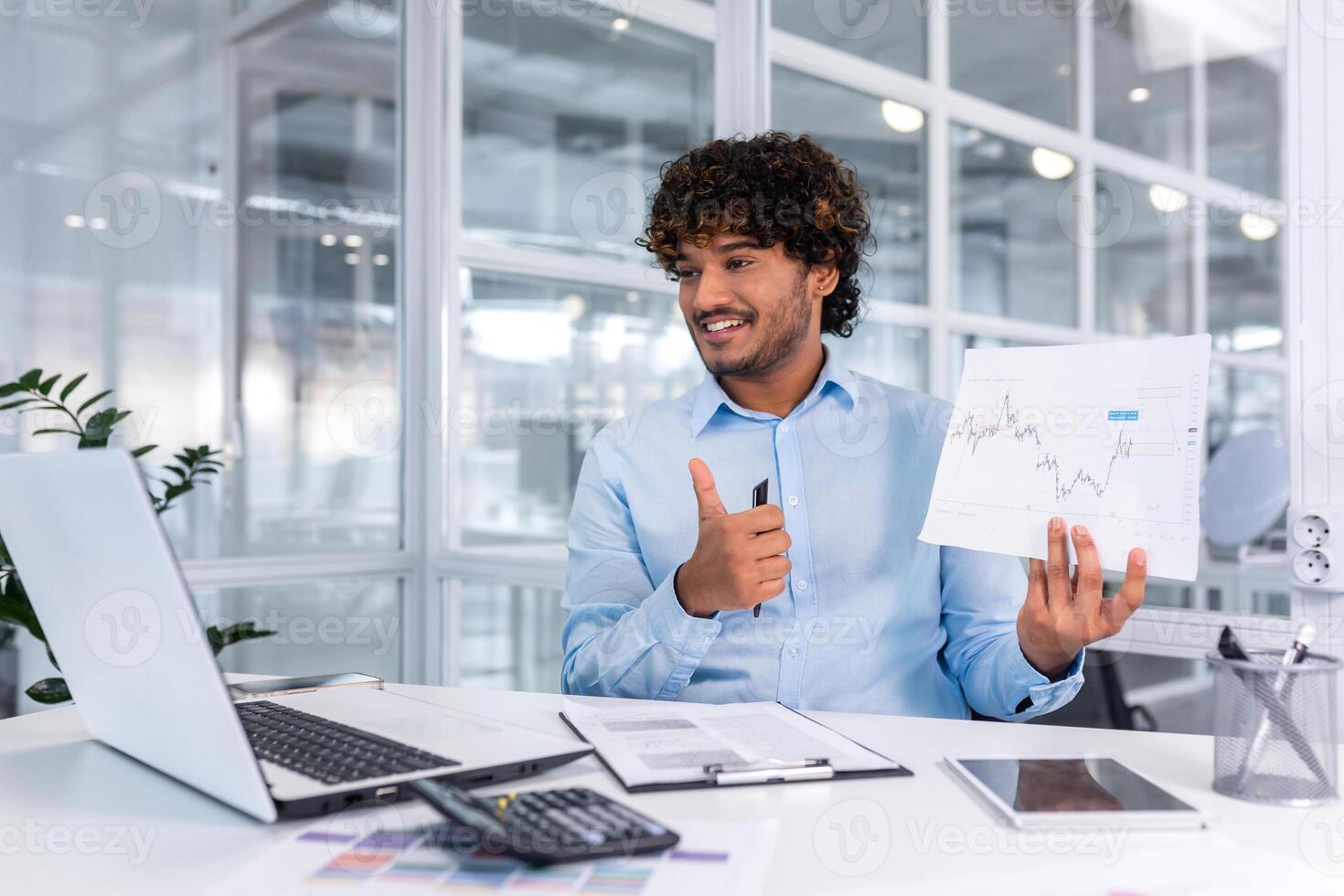 Online meeting of business partners, businessman shows web camera laptop graph with good financial results and smiles, Hispanic man works with documents financier inside office. photo