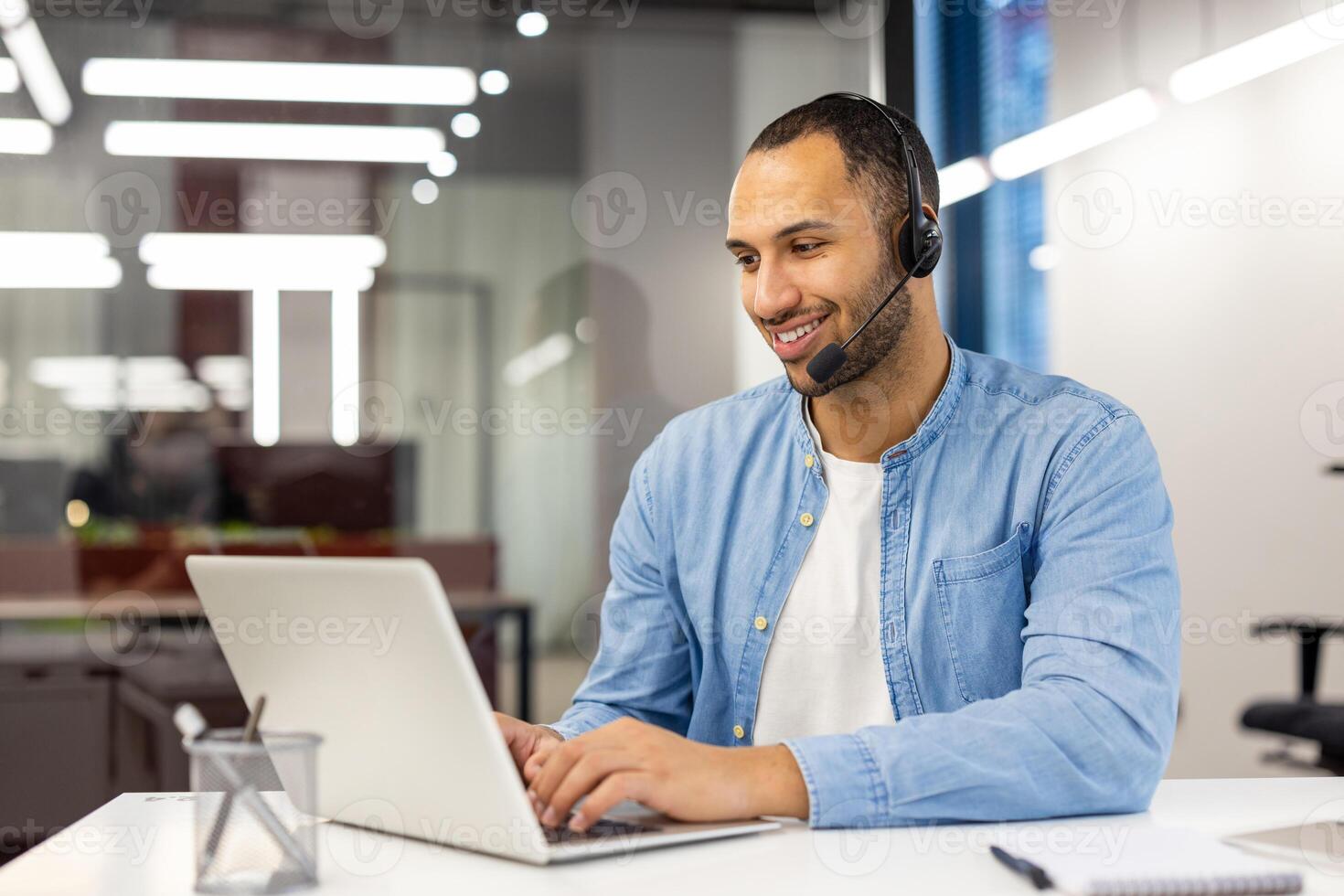 contento masculino cliente Servicio agente con un auriculares trabajando a un computadora en un moderno oficina configuración, atractivo en cliente apoyo. foto