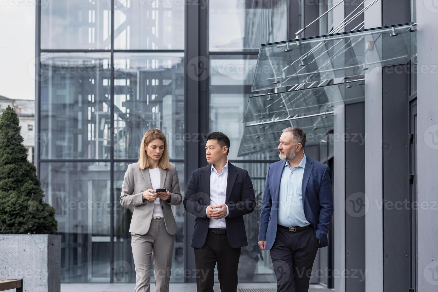 Diverse business group, three male and female workers walking and chatting discussing plans, outside office building photo