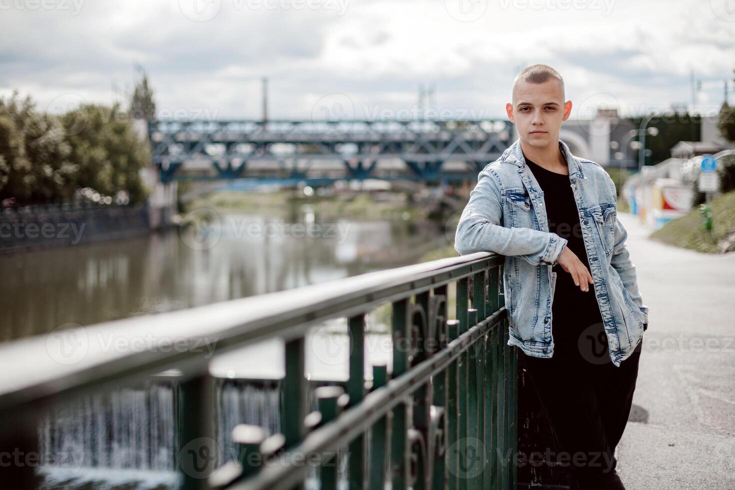 A man in a black shirt and blue jacket stands on a bridge railing photo