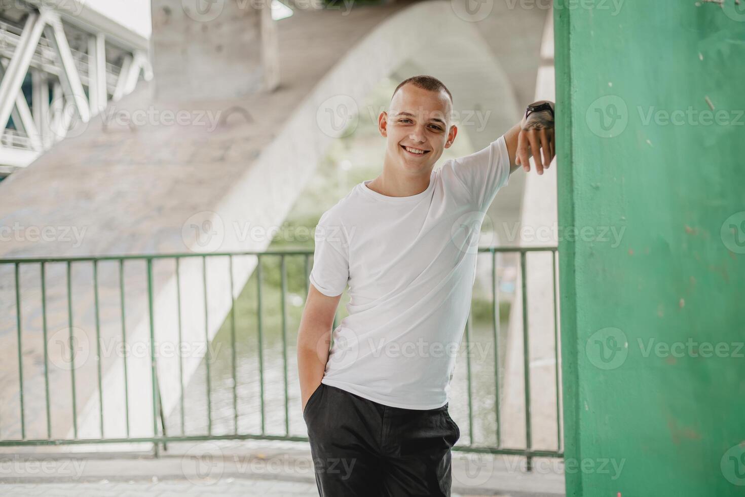 A man in a white shirt stands on a bridge with his arms crossed photo