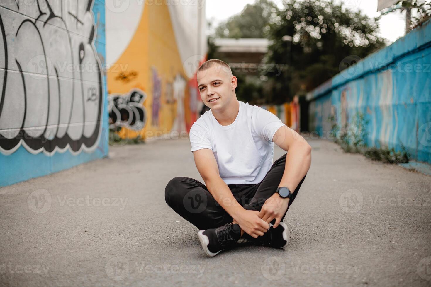 A young man sits on the ground with his hands on his knees photo