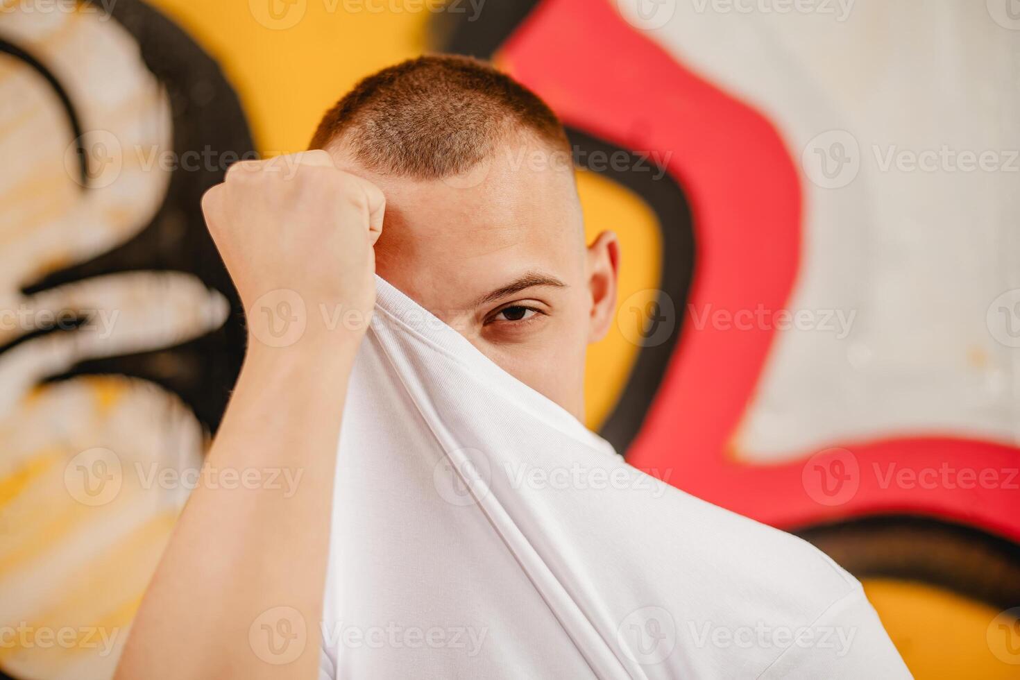 A man with a shaved head is hiding his face behind a white shirt photo