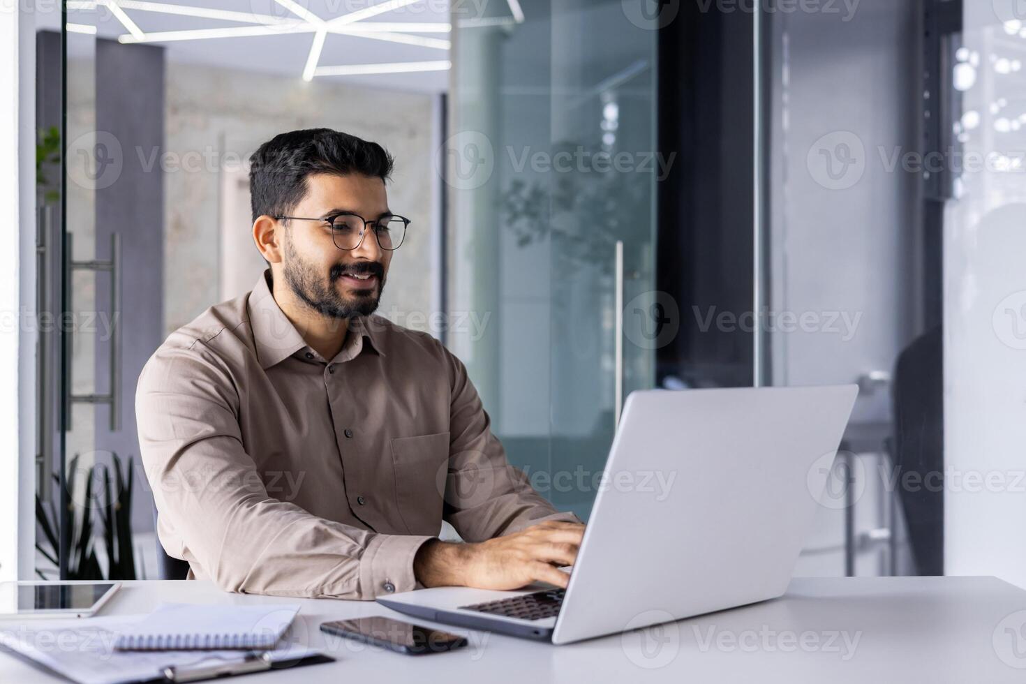 empresario contento exitoso y sonriente trabajando con ordenador portátil dentro oficina a lugar de trabajo, hombre satisfecho con financiero resultado prepara informe, contador financiero mecanografía en computadora teclado. foto