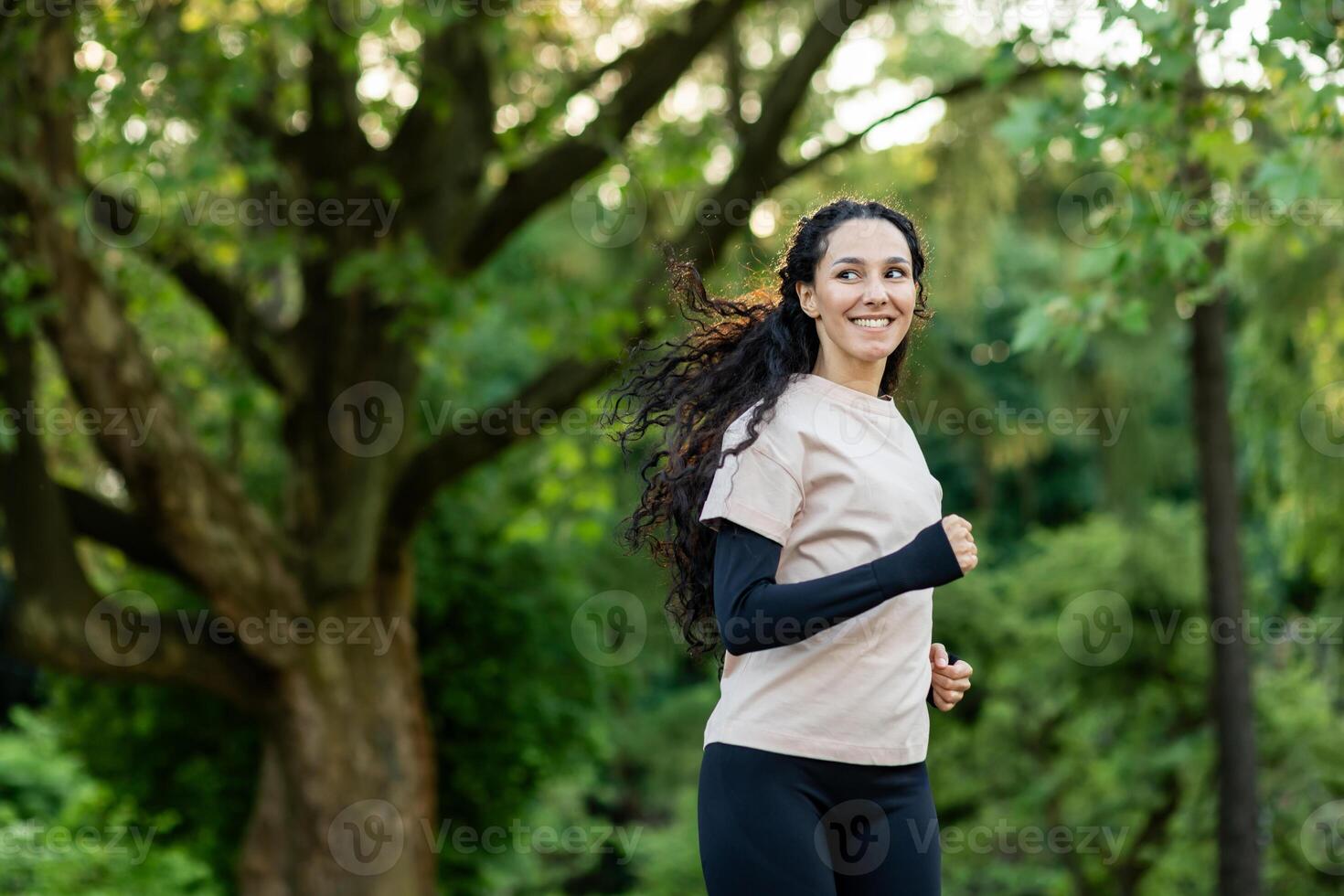 Young beautiful woman running in the evening in the park, hispanic woman with curly hair smiling contentedly, active lifestyle photo