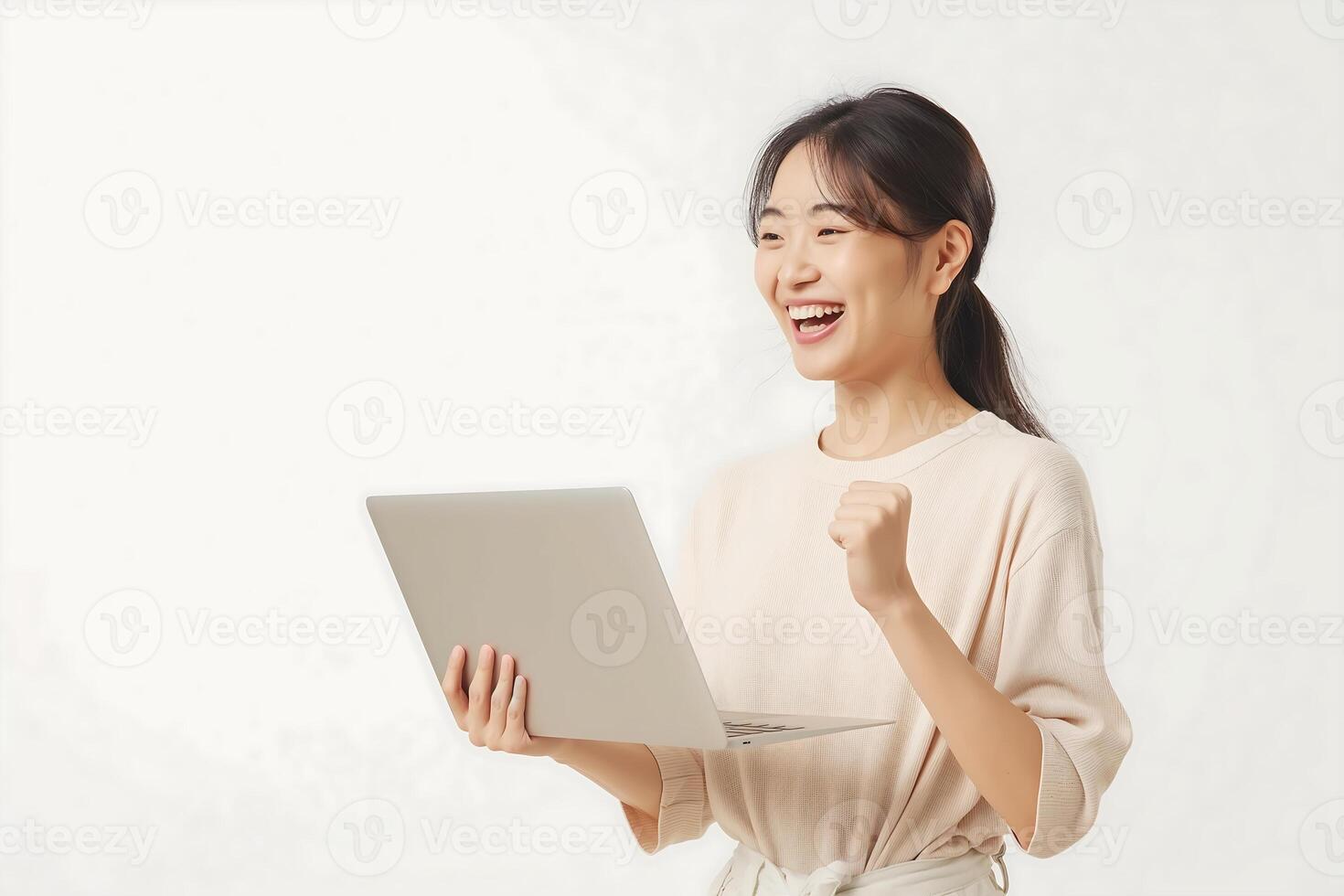 A young Asian woman stands holding a laptop with an expression of joy photo