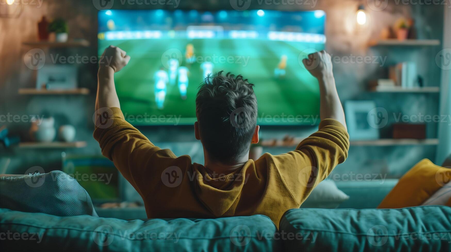 Happy man sits on the sofa with his back facing the TV which is showing a football match photo