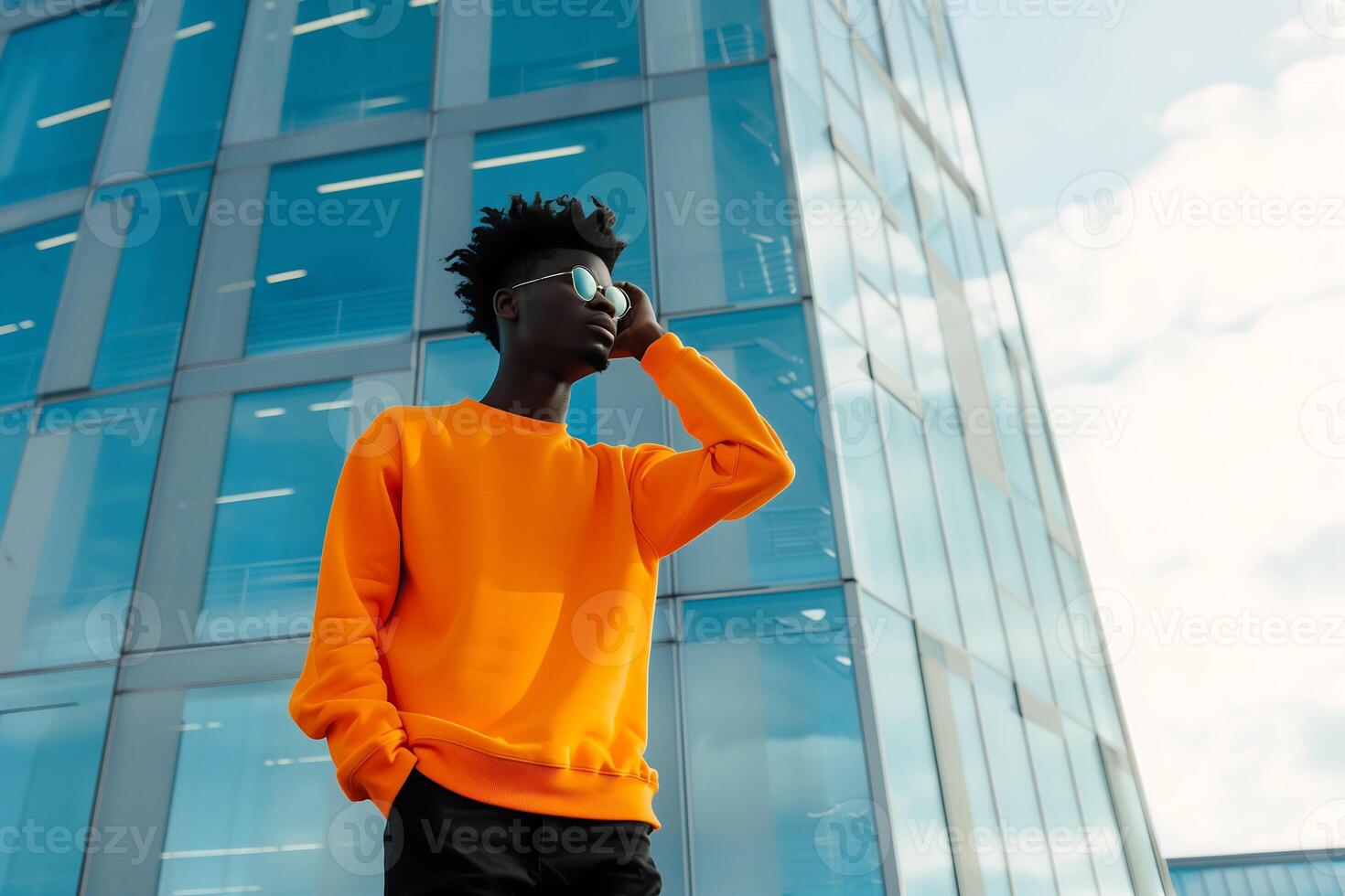 Portrait of an attractive black afro American male model wearing orange blank mockup crewneck sweatshirt and posing In front of a modern office building exterior photo