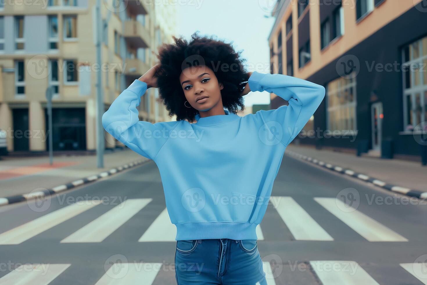 Portrait of an attractive black afro American female model wearing powder blue blank mockup crewneck sweatshirt and posing in the middle of the pedestrian crossing photo