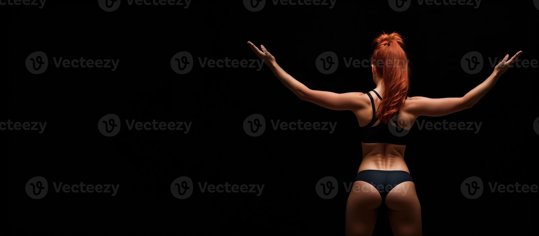athletic redhead girl in sports underwear on a black background, rear view banner photo