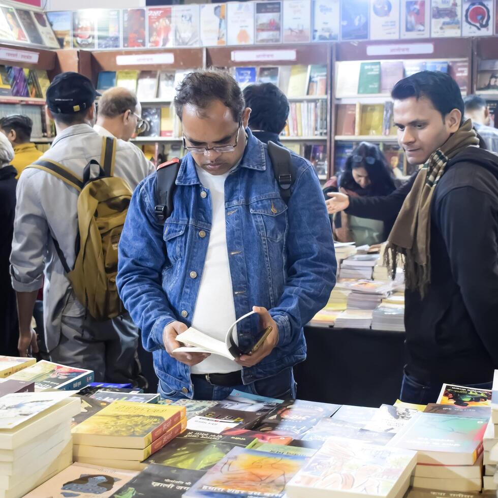 Delhi, India, February 17 2024 - Various age group people reading variety of Books on shelf inside a book-stall at Delhi International Book Fair, Books in Annual Book Fair at Bharat Mandapam complex photo