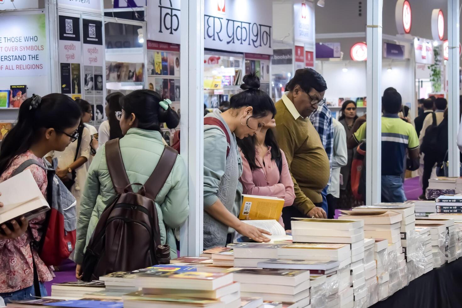 Delhi, India, February 17 2024 - Various age group people reading variety of Books on shelf inside a book-stall at Delhi International Book Fair, Books in Annual Book Fair at Bharat Mandapam complex photo