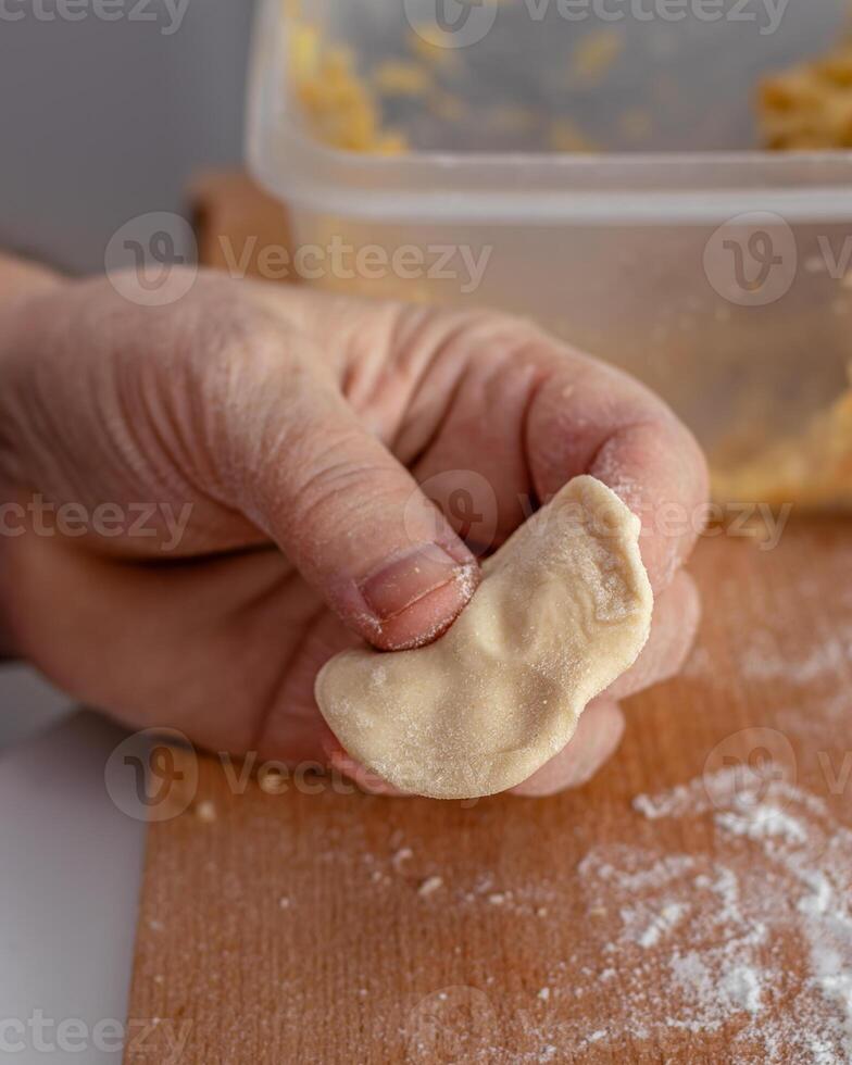 Woman hands are making a damp dumpling. On the wooden counter photo