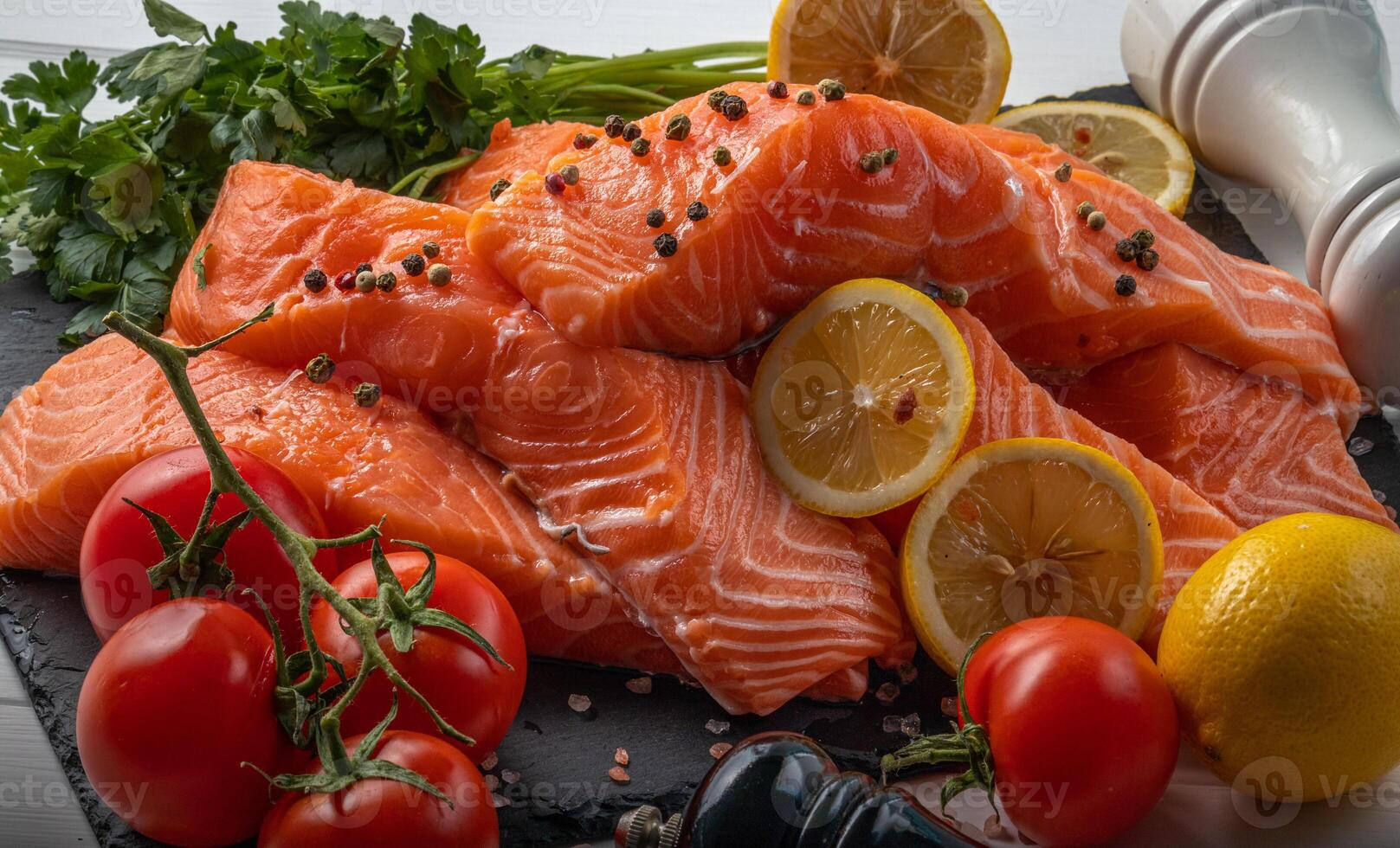 Fresh raw salmon fillet with cooking ingredients, herbs and lemon on black slate photo
