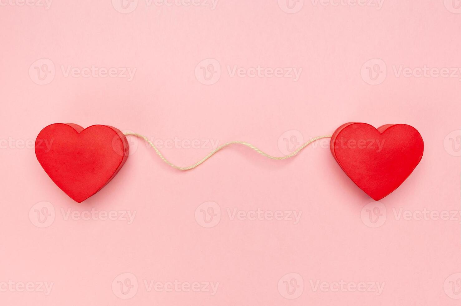 Pair of red hearts connected with a string of twine photo