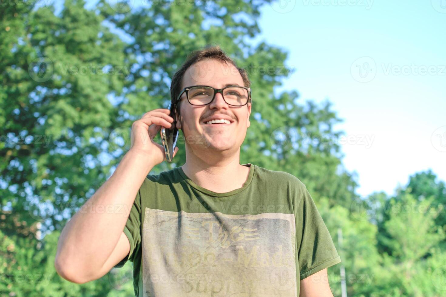 Young man with eyeglasses and green t-shirt talking on cell phone at the park photo