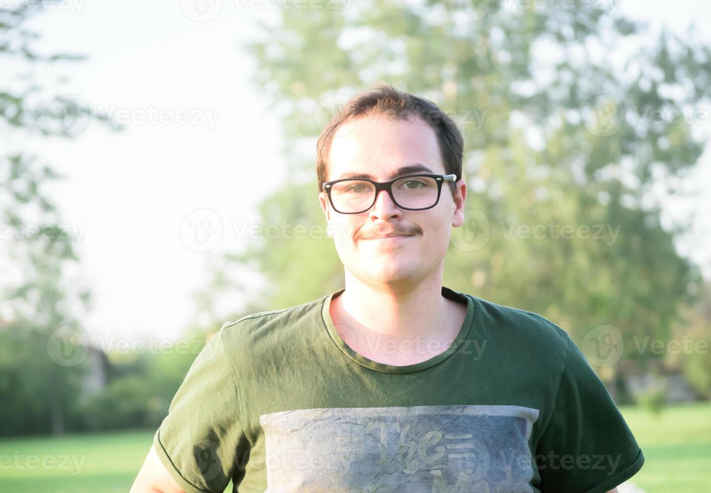 joven hombre con lentes en parque mirando a cámara contento foto