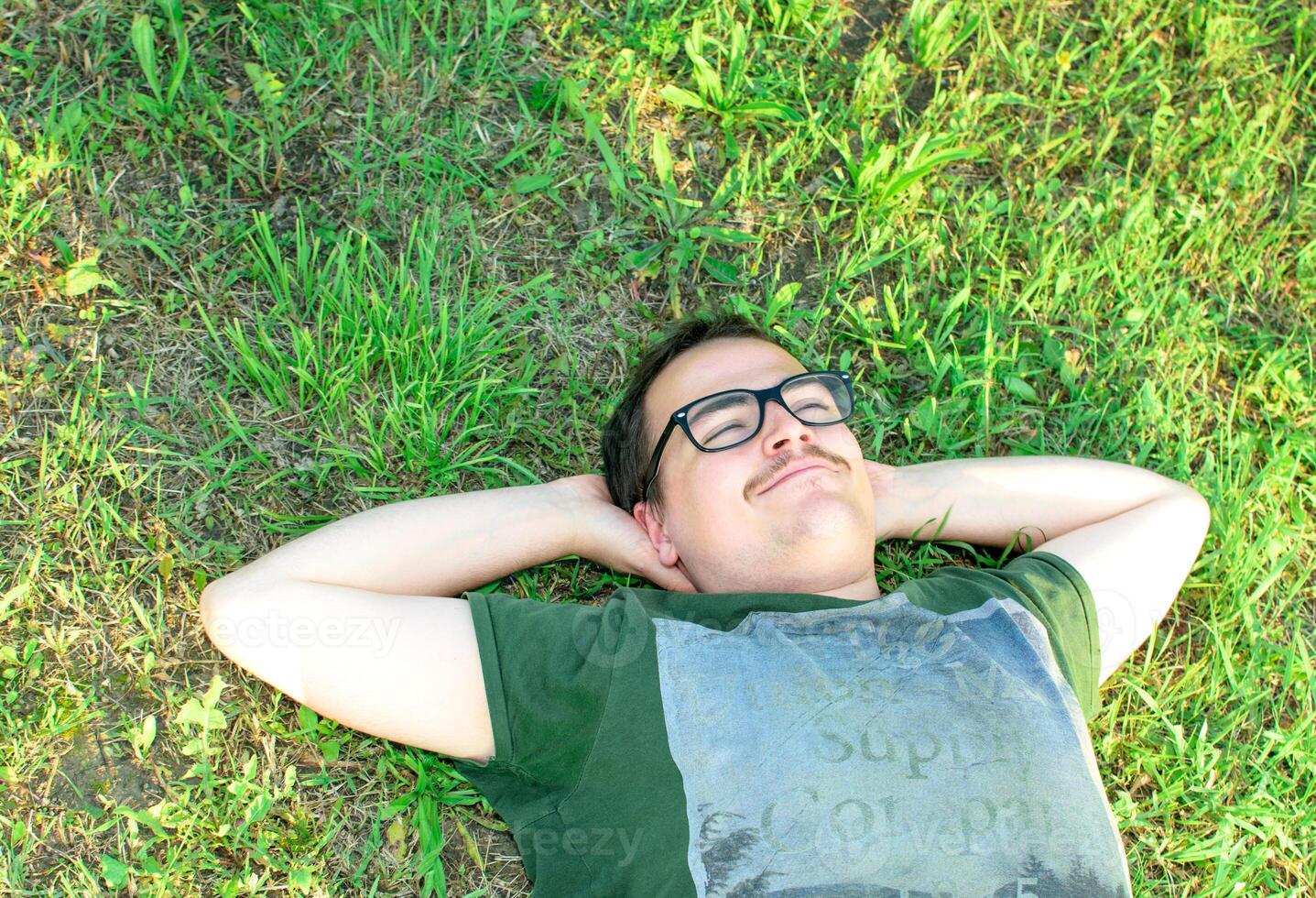 Young man with glasses lied on grass enjoying vacation after studying very happy photo